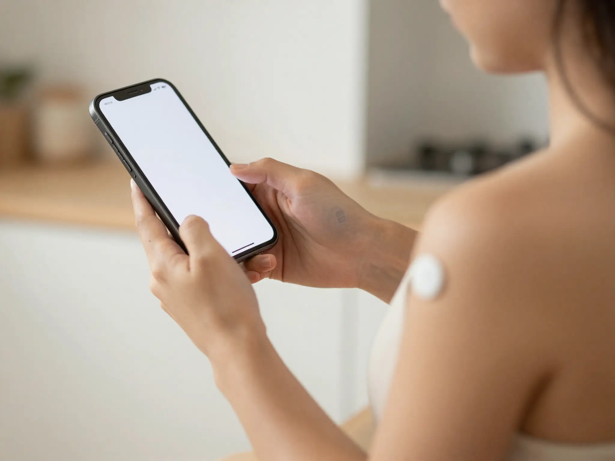 A person checking glucose on a phone with a CGM sensor on their arm